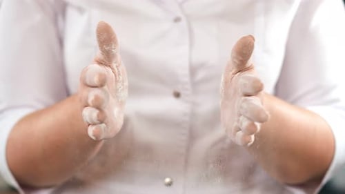 Frau in weißer Uniform klatscht in den Händen, bedeckt mit Mehl, Zeitlupe