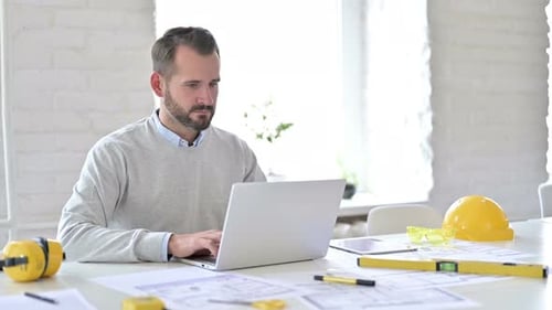 Serious Young Male Architect Using Laptop in Office