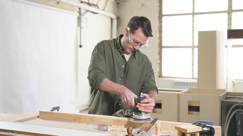Young Male Joiner Working with Wood Using Electric Sander in Workshop
