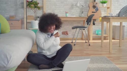 Belle femme afro-américaine avec une coiffure afro assise sur le sol avec un ordinateur portable appris