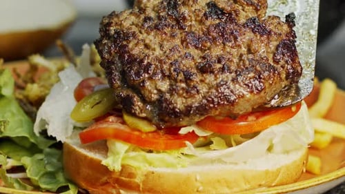 Large hamburger placed on a bun with vegetables in slow motion
