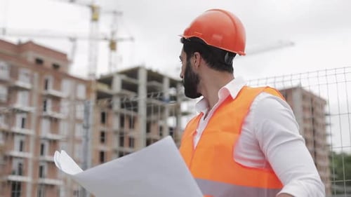 Bauingenieur hält ein Projekt in der Hand. Er überprüft eine Zeichnung auf der Baustelle