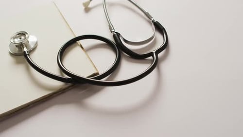 Video of close up of stethoscope with notebook on pink background