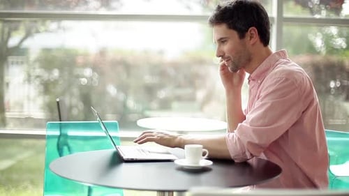 Man using laptop computer and talking on cell phone in cafe
