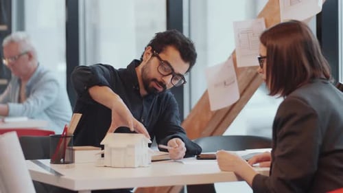 Male and Female Architects Discussing House Model in Office