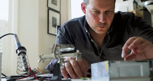 Man Repairs Electronics at Table Indoors