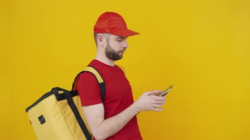 Junger positiver Zusteller verwendet Smartphone, genehmigt App und zeigt Gadget mit Chroma-Key-Bildschirm