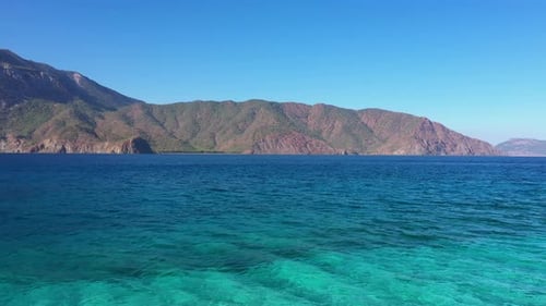 Türkisfarbene Meeresbucht mit Bergen und blauem Himmel im Hintergrund