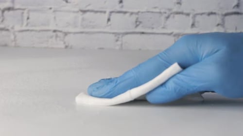 Gloved Hand Cleaning White Surface with Wipe