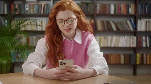 Attractive Student Woman Holding Modern Smartphone Texting Message in Home Office or Library