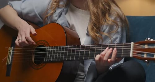 Blonde Woman Playing Guitar on Couch with Headphones
