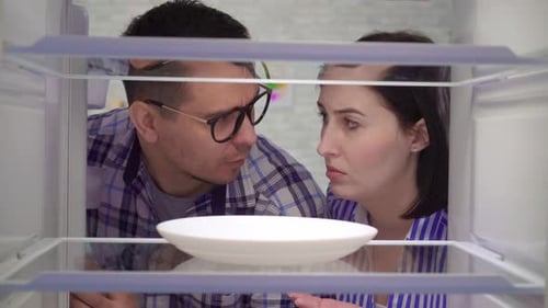 Couple Stares at Empty Refrigerator with Concern