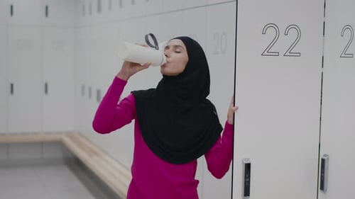 Athletic Woman Drinks Water in Locker Room