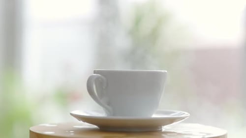 Ein Zuckerwürfel fällt in eine Kaffeetasse und spritzt, zerstreut und Dampf geht