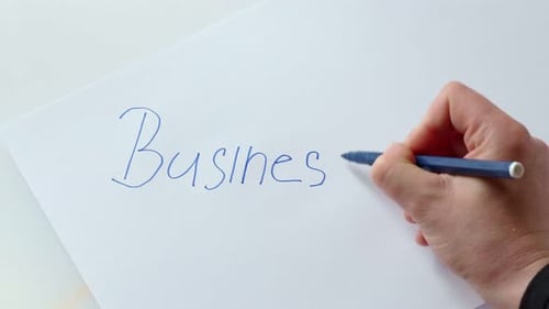 Top view. Woman writes the word BUSINESS with blue pencil on paper.