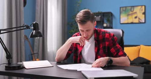 Thoughtful Young Adult Studying Financial Documents Indoors