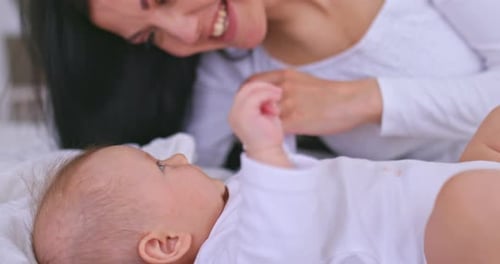 Smiling Woman Playing with Baby on White Bed
