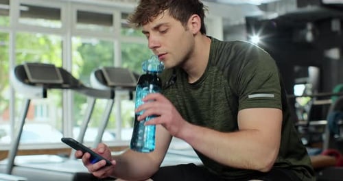 Sportsman Using Phone and Drinking Water in Gym