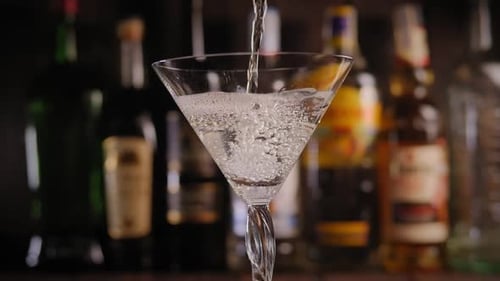 Martini Being Poured Into a Glass in Bar Against a Background of Blurred Bottles