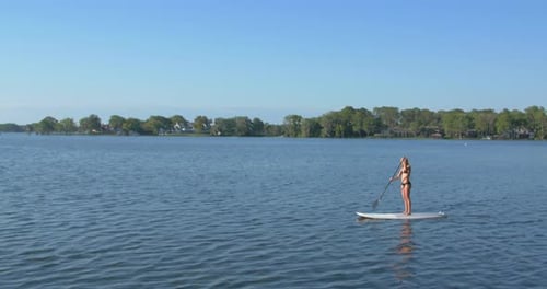 A young woman sup stand-up paddleboarding on a lake.