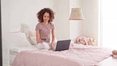 Woman Shopping Online in Bedroom With Credit Card