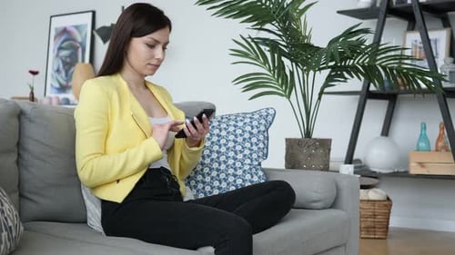 Young Woman Using Smartphone on Couch at Home