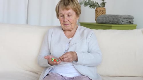 Senior Woman Inspecting Pills in Hand Indoors
