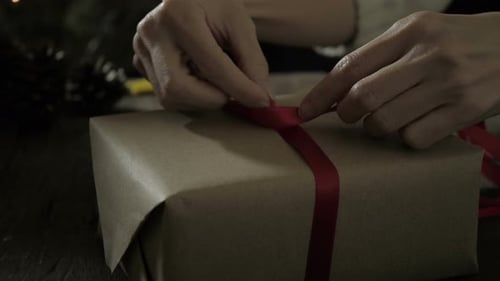 Hands Tying Red Ribbon on Gift