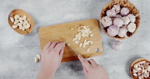 Men's Hands Cut the Garlic Into Pieces on a Wooden Cutting Board.
