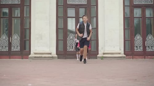 Three Happy Children Running From School After Studying. Wide Shot Portrait of Cheerful Caucasian