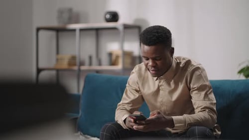 Man Smiling while Using Smartphone on Sofa Indoors