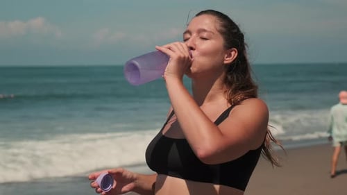 Woman Drinks Water Bottle on Sunny Beach