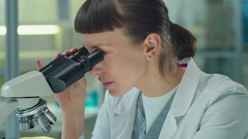 Focused Scientist Using Microscope in Bright Laboratory