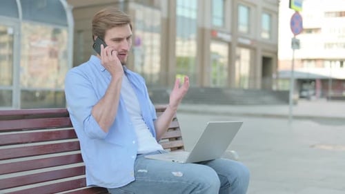 Man Uses Laptop and Phone on City Bench