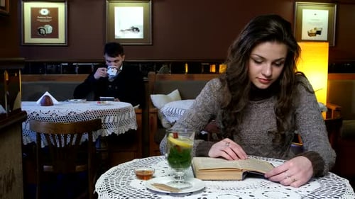 Beautiful Girl with Handsome Guy in a Cafe, She Reads Book and He Uses Tablet Computer.