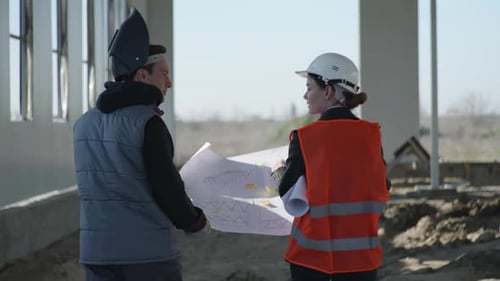 Male and Female Industrial Engineers in Protective Suits and Helmets Who Are Discussing Construction