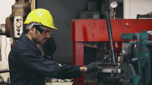 Factory Worker Talking on Portable Radio While Inspecting Machinery Parts