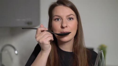 Woman in Kitchen Samples Food with Spoon