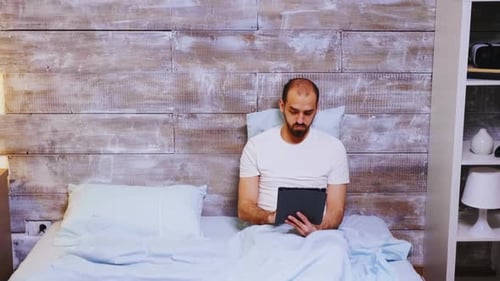 Man Uses Tablet Computer While Sitting in Bed