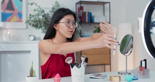 Mujer asiática con gafas presenta un tutorial de maquillaje que muestra a los espectadores a la cámara del teléfono