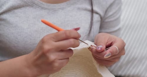 Woman Crocheting with White Yarn and Orange Needle