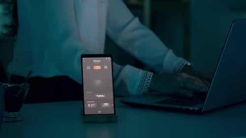 Woman Uses Laptop with Smart Home App on Phone