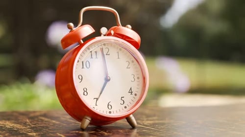 Old vintage red alarm clock shaking and ringing on a garden table. 4KHD