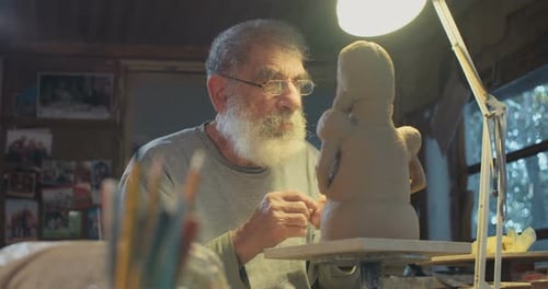 Old sculptor working on a clay sculpture in his small studio