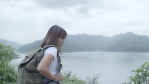 Hiker backpacker woman on hiking adventure feeling freedom walking in forest near lake in rainy day.