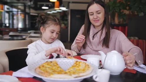Mujer con hija pequeña en un restaurante solo come pizza de queso cocido