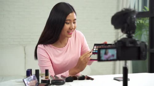 La bloguera de belleza presenta cosméticos de belleza mientras está sentada frente a la cámara para grabar un vídeo con un cepillo.