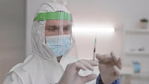 Health Worker Inspecting Syringe in Protective Suit