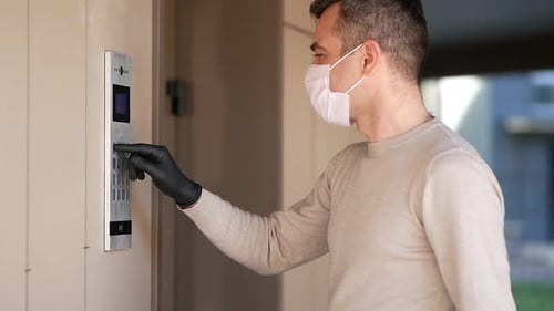 Un homme portant un masque facial et des gants compose le Code sur l'interphone et entre dans le porche de son appartement