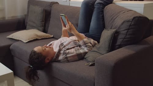 Woman Relaxing on Couch Using Smartphone at Home